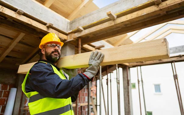 construction worker with hard hat carrying lumber through demo home